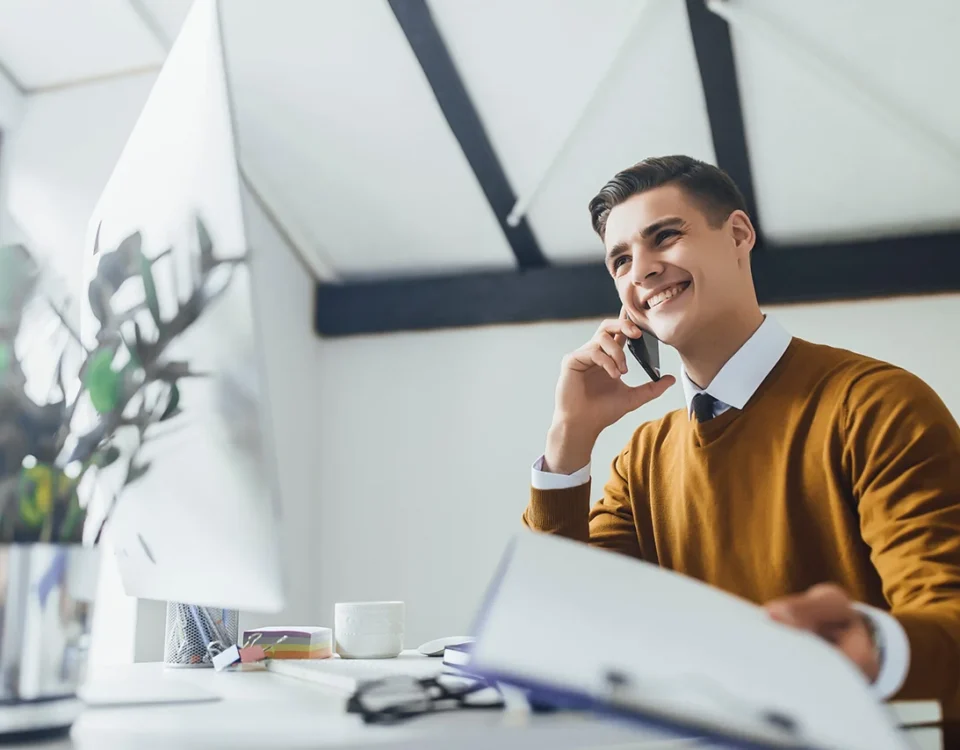 Young brunette smiling businessman with papers, speaking at his phone in modern office.