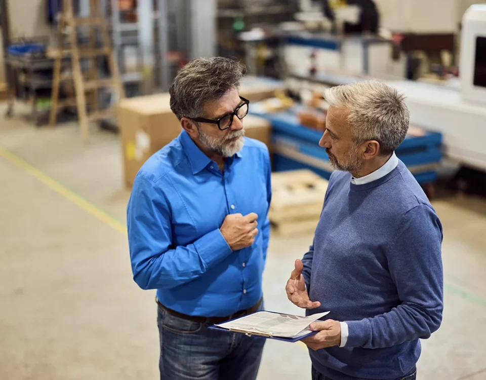Two mature professionals engage in discussion within an industrial workplace setting